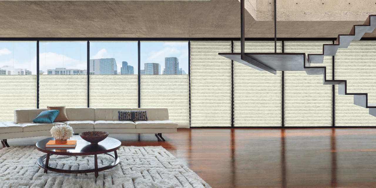 Large living room with a sofa and coffee table set in front of many picture windows with Vignette Modern Roman Shades running bottom to top and top to bottom.